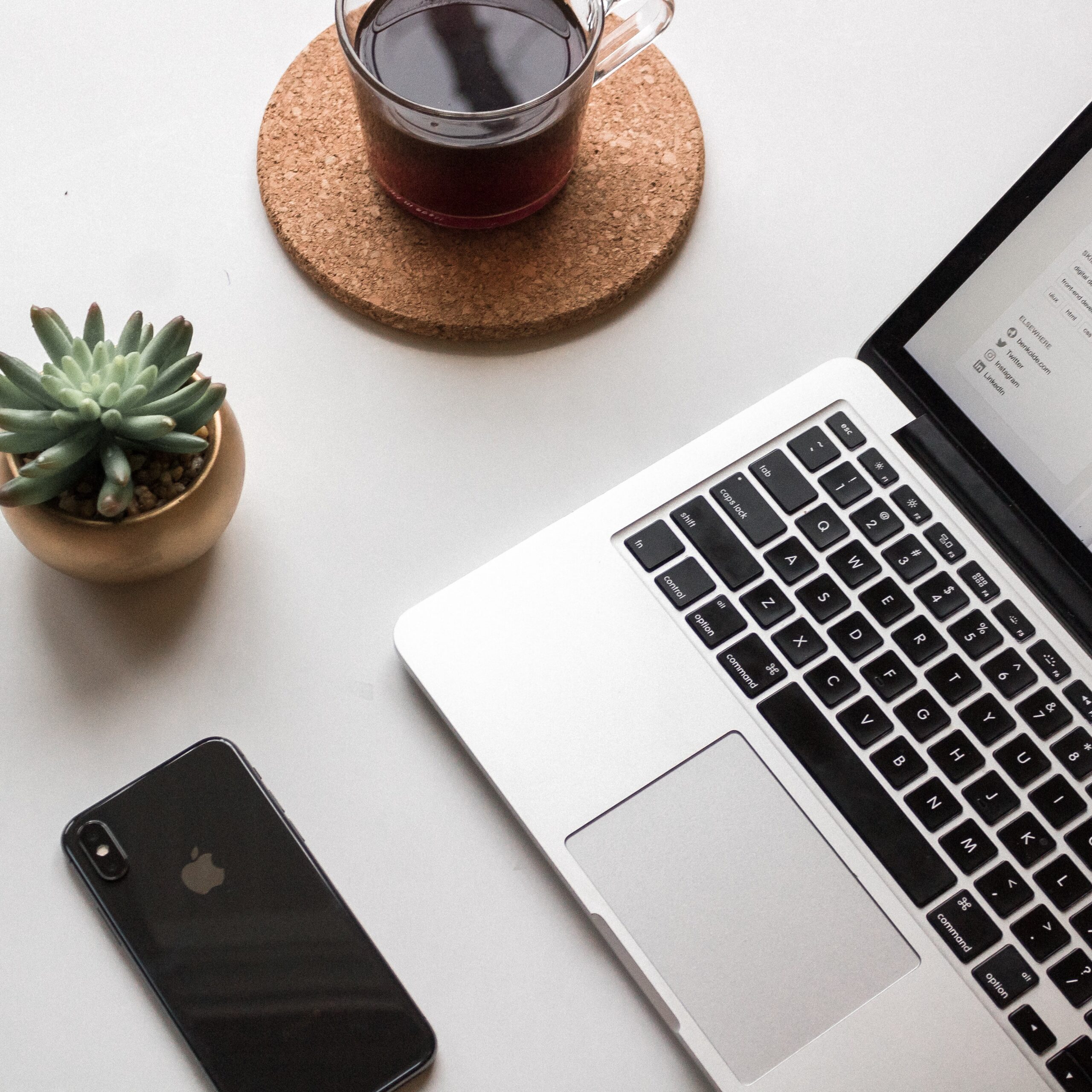 A laptop, computer, and cactus along with a drink.