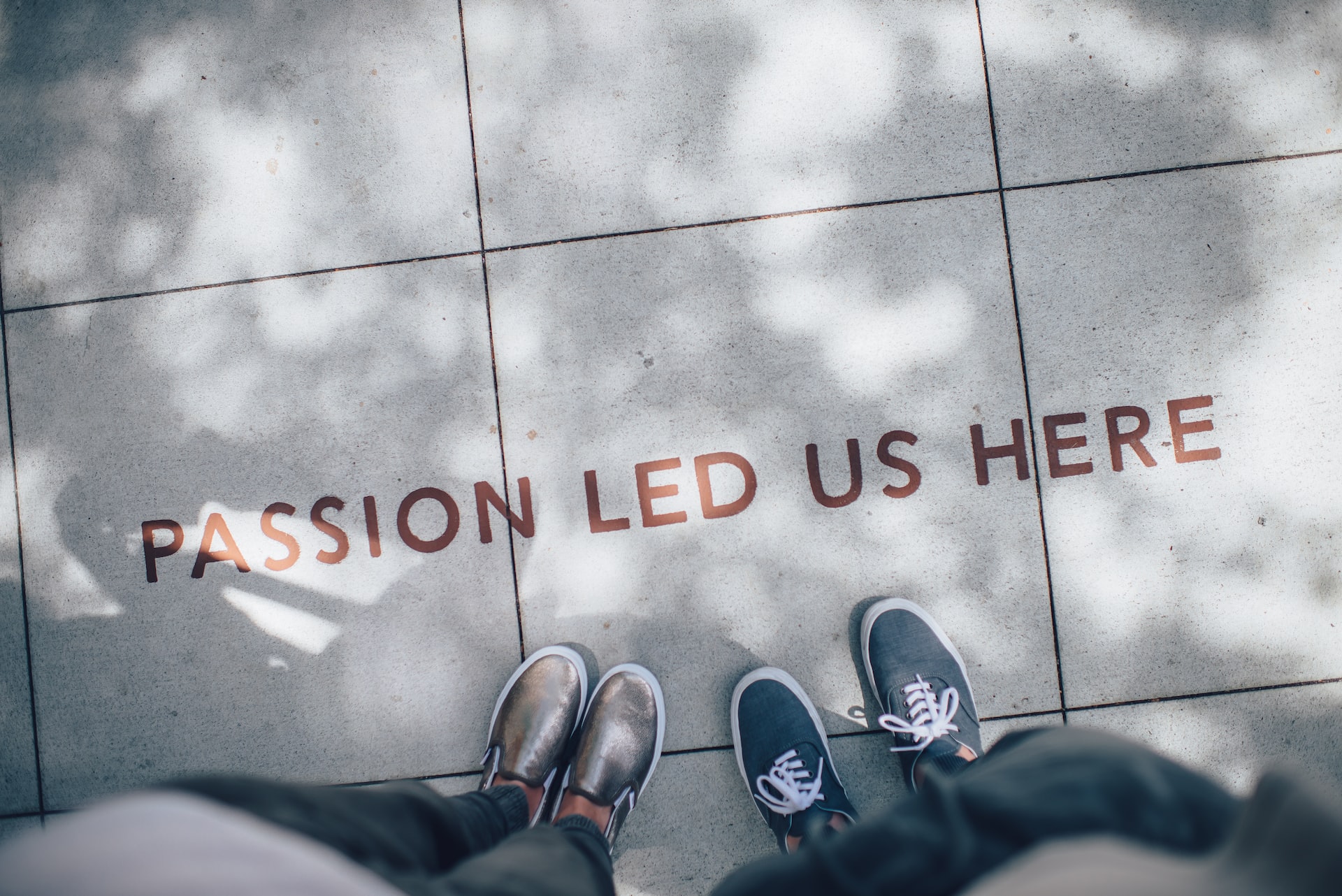 Two pairs of feet near an inscription on the ground that says: "Passion led us here"